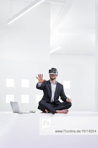 Businessman wearing VR glasses in office next to laptop