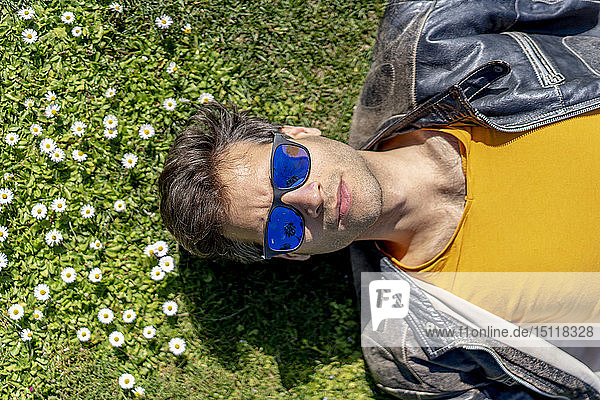 Auf Blumenwiese liegender Mann mit Sonnenbrille