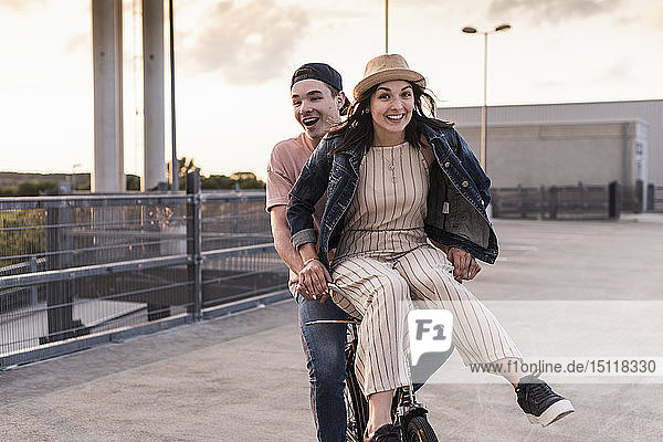 Glückliches junges Paar zusammen auf einem Fahrrad auf dem Parkdeck
