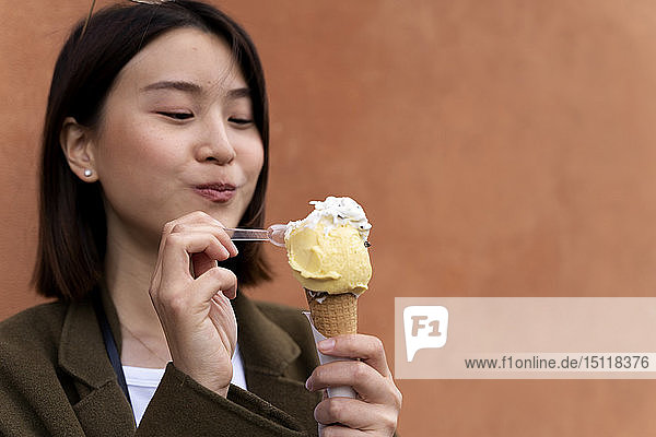 Porträt einer jungen Frau  die an einer Orangenwand eine Eistüte isst
