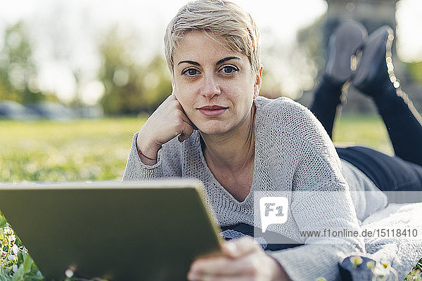 Porträt einer auf einer Wiese liegenden jungen Frau mit digitalem Tablett