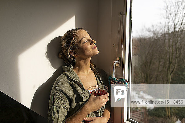 Junge Frau am Fenster genießt den Sonnenschein