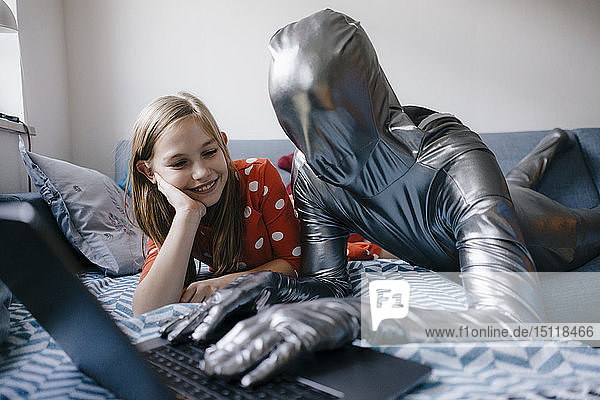 Man in morphsuit and girl lying on couch at home using laptop