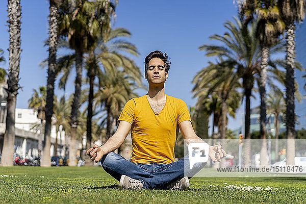 Spanien  Barcelona  Mann praktiziert Yoga auf dem Rasen in der Stadt