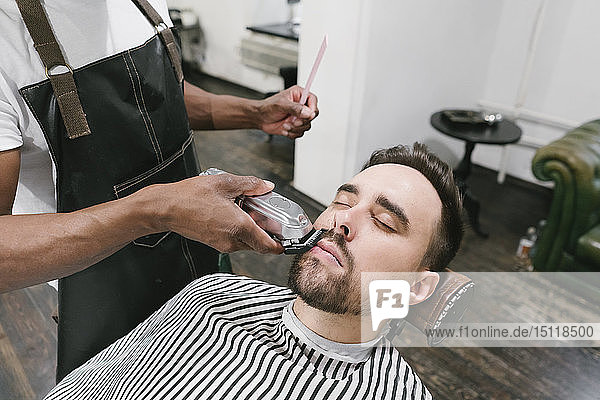Barber cutting beard of a customer in barber shop