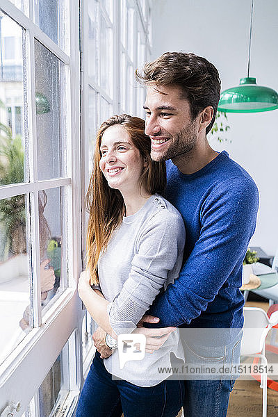 Glückliches  liebevolles Paar  das sich zu Hause am Fenster umarmt