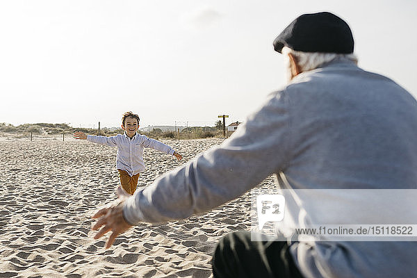 Happy little boy running into his grandfather's arms on the beach