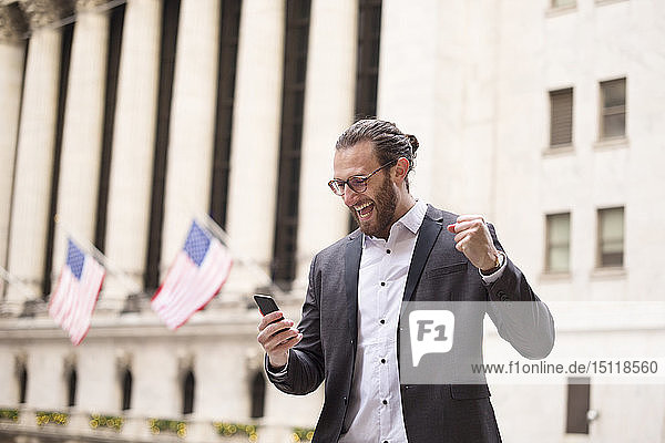 Aufgeregter junger Geschäftsmann schaut auf Handy vor der Börse  New York City  USA