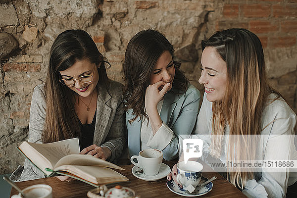 Three happy young women reading a book in a cafe