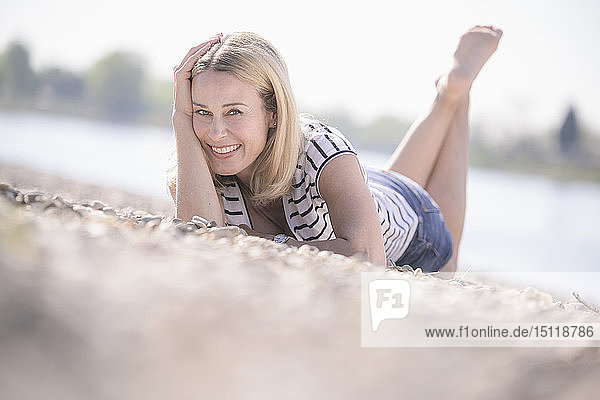Lächelnde reife Frau liegt auf Kieselsteinen am Flussufer
