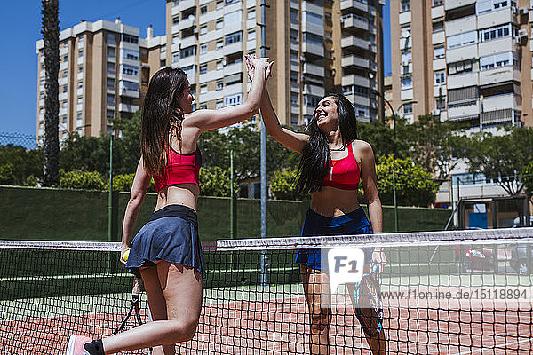 Zwei glückliche Tennisspielerinnen mit High Fiving am Netz