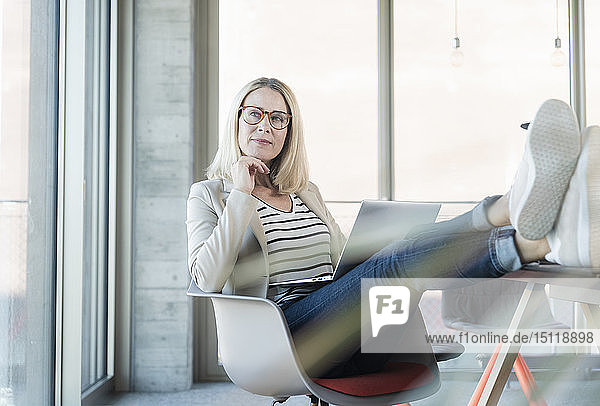 Entspannte Geschäftsfrau mit Laptop im Büro mit hochgelegten Füßen