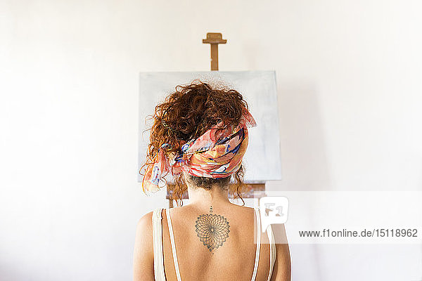 Rückansicht einer jungen Malerin im Kunstatelier vor leerer Leinwand