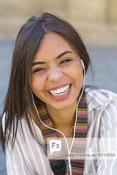 Porträt einer lachenden jungen Frau  die mit Kopfhörern Musik hört