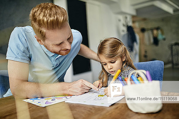Vater und Tochter sitzen am Tisch und malen ein Malbuch