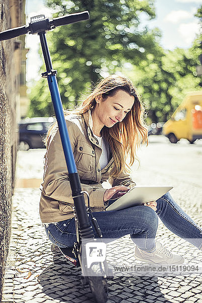 Lächelnde Frau sitzt auf E-Scooter mit digitalem Tablet