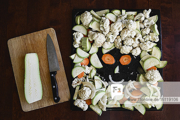 Funny face made of sliced vegetables on baking tray