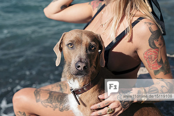 Spanien  Mallorca  Porträt eines Hundes  der neben einer tätowierten Frau vor dem Meer sitzt