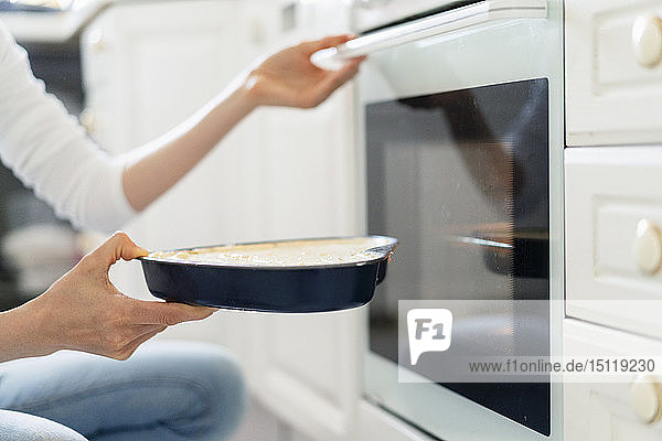 Nahaufnahme einer Frau  die Kuchenteig in den Ofen schiebt