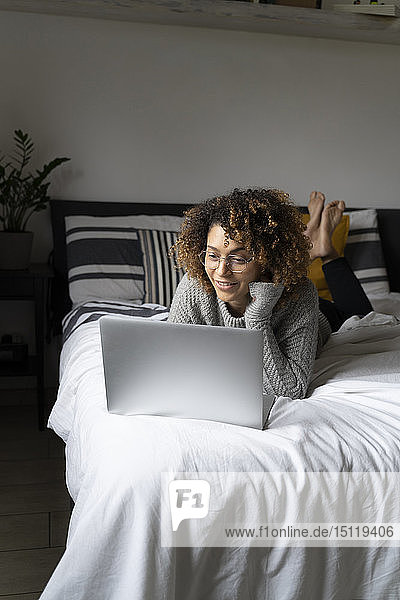 Frau  die auf dem Bett liegt  einen Laptop benutzt und im Netz surft