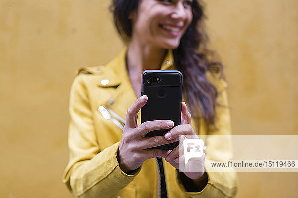 POrtrait einer jungen Frau  die eine gelbe Lederjacke trägt und eine Selfie nimmt  gelbe Wand im Hintergrund