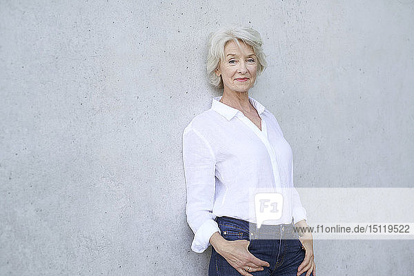Porträt einer entspannten reifen Frau in weißem Hemd  die gegen eine Betonwand lehnt