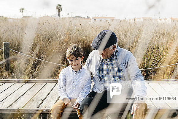 Großvater sitzt mit seinem Enkel an der Strandpromenade und entspannt
