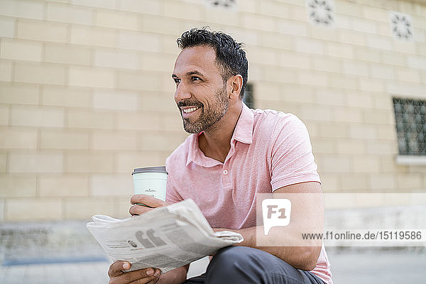 Lächelnder Mann mit Kaffee und Zeitung zum Mitnehmen in der Stadt