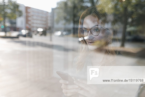 Selbstbewusste Geschäftsfrau hinter Fensterscheibe mit Handy