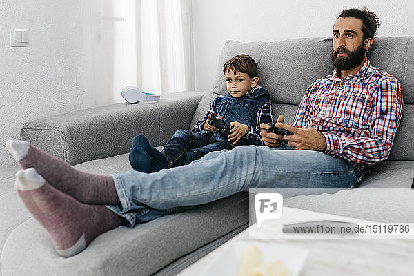 Portrait of father and son sitting together on the couch playing computer game