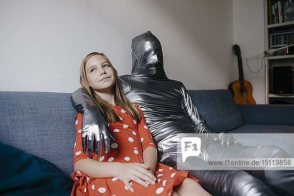 Mann im Morphsuit und Mädchen sitzen zu Hause auf der Couch