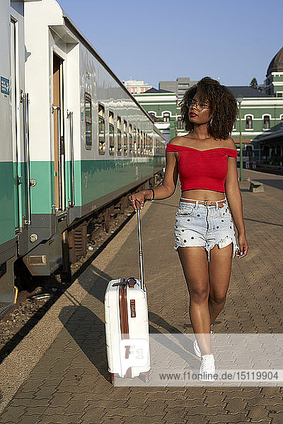 Frau geht mit ihrem Koffer am Bahnhof