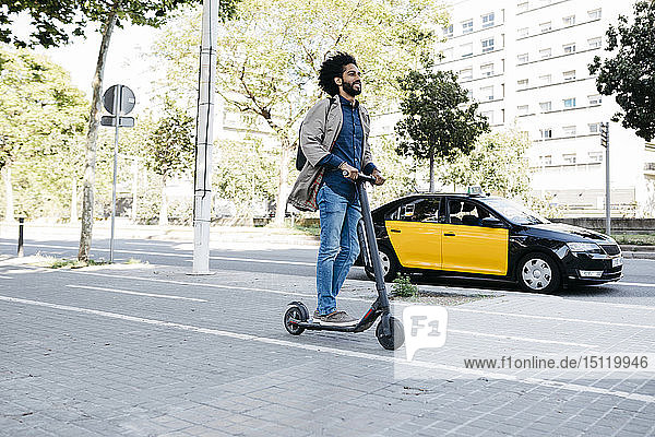 Mann mit Rucksack fährt mit seinem E-Scooter auf einem Fahrradweg