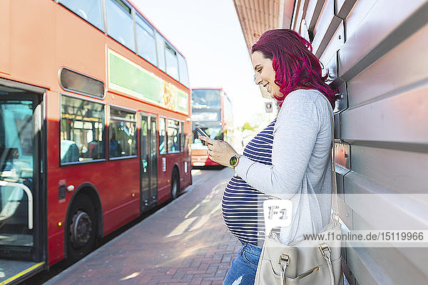 Schwangere Frau benutzt ihr Telefon an der Bushaltestelle