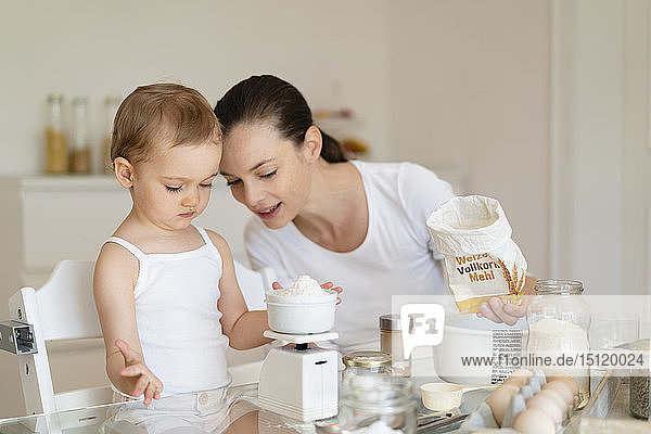 Mother and little daughter making a cake together in kitchen at home weighing flour