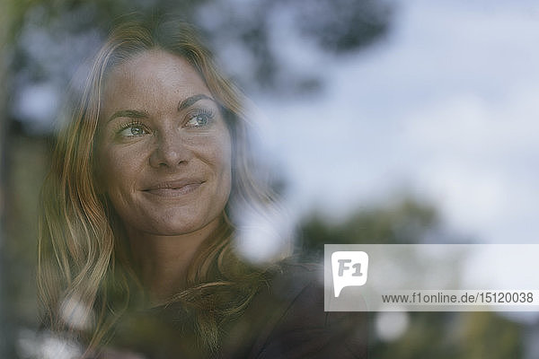Lächelnde junge Frau hinter Fensterscheibe