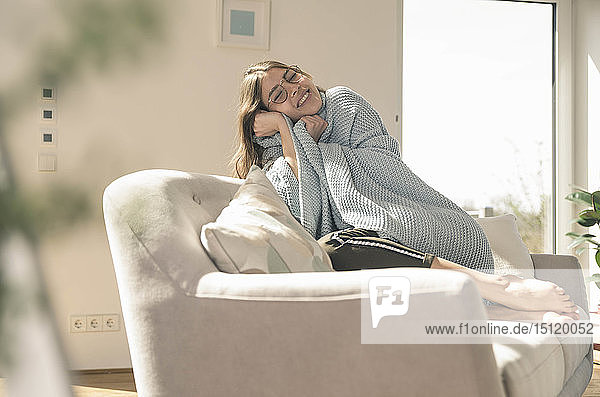 Glückliche junge Frau mit Wolldecke auf dem Sofa