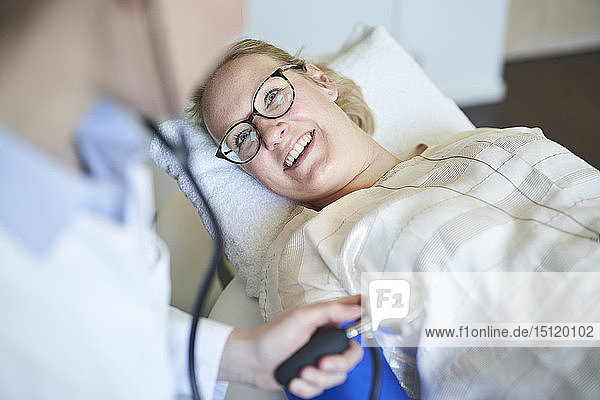 Lächelnder Patient schaut den Arzt an  der in der medizinischen Praxis den Blutdruck misst