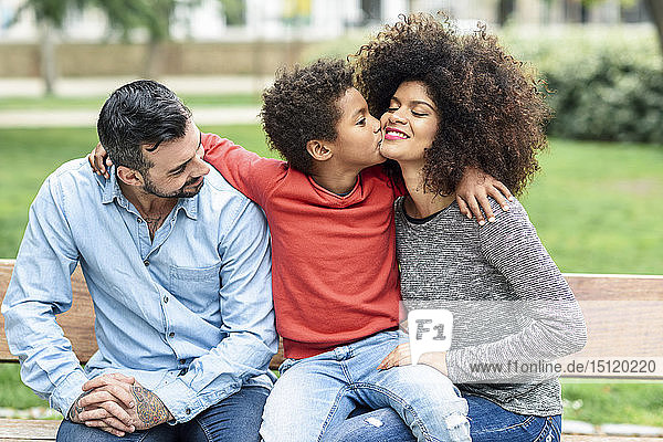 Familie sitzt auf einer Parkbank  Sohn küsst Mutter