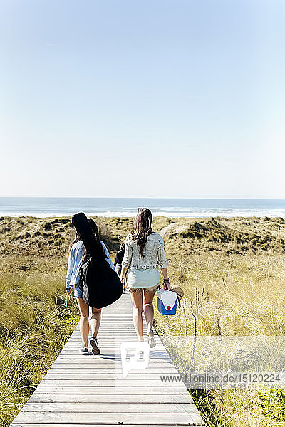 Rear view of women with guitar bag walking in dunes towards beach