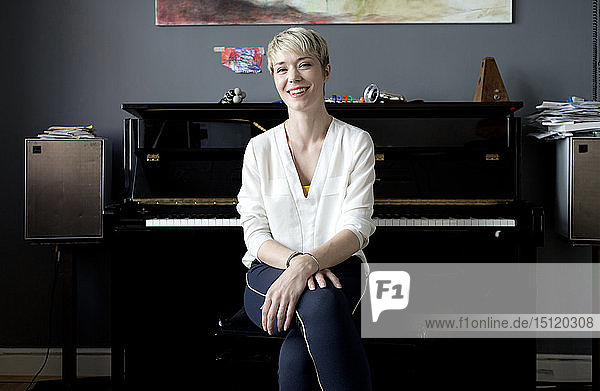 Porträt einer lachenden Frau  die in ihrem Musikzimmer vor dem Klavier sitzt