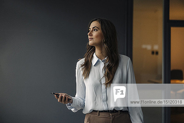 Young businesswoman holding cell phone looking sideways