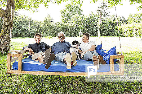 Männer einer Familie sitzen auf einem Schaukelbett im Garten und unterhalten sich