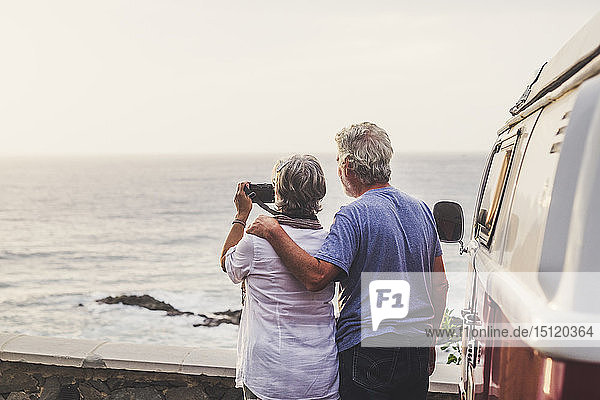Älteres Ehepaar reist in einem Oldtimer-Van und fotografiert am Meer