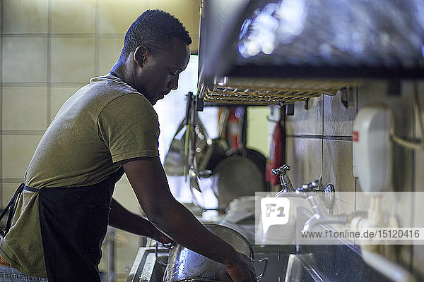 Junger Mann beim Geschirrspülen in der Restaurantküche  Südafrika