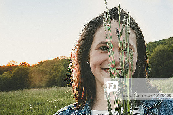 Porträt einer lächelnden Teenagerin mit Gräsern bei Sonnenuntergang