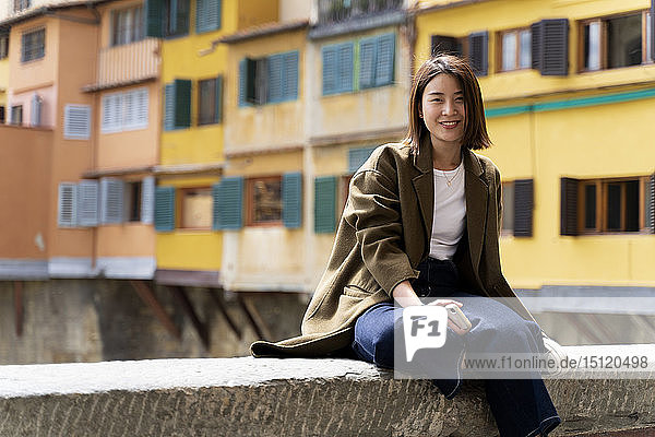 Italien  Florenz  lächelnde junge Frau ruht auf einer Mauer in der Stadt