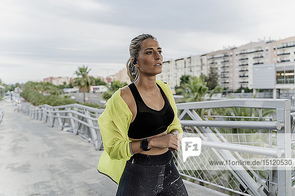 Sportler mit Kopfhörern und Smartwatch auf einer Brücke in der Stadt