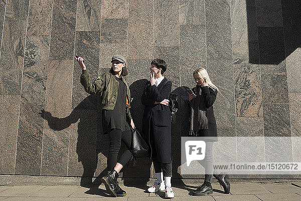 Drei junge Frauen stehen an einer Mauer in der Stadt und unterhalten sich