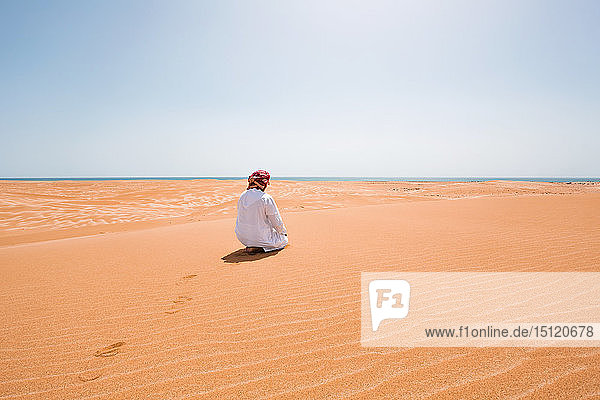 Bedouin in National dress praying in the desert  rear view  Wahiba Sands  Oman